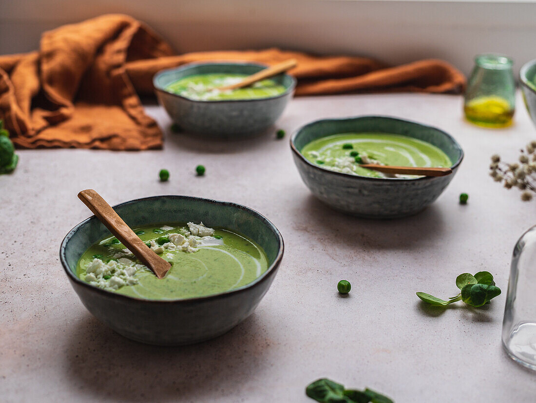 Pea cream soup in bowls served on table with napkin and vase with flowers