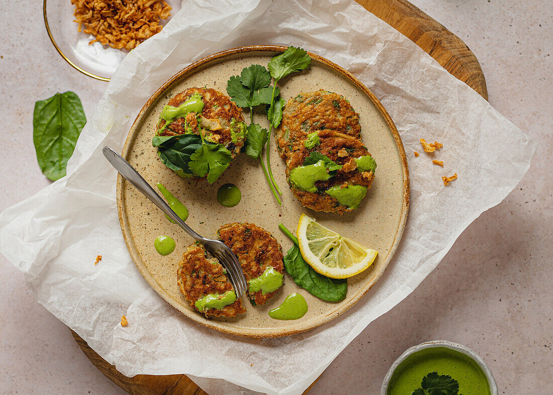 Herbal fritters with green sauce and lemon slice served on wooden board and craft paper