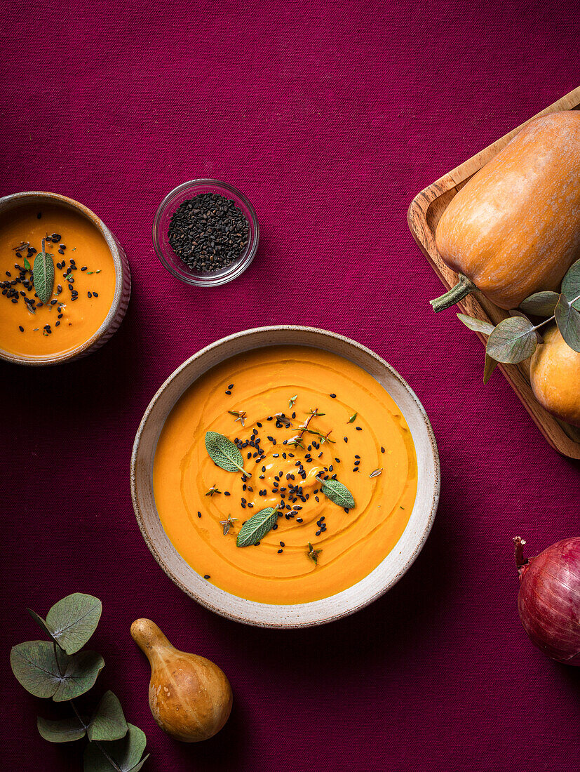 Bowl with delicious pumpkin soup served with seasonings placed near fresh pumpkin on purple table