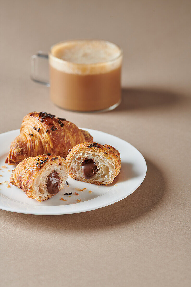 Sweet croissants with chocolate placed on white plate near blurred cup of coffee