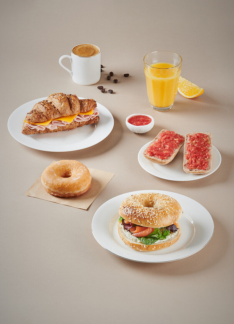 Sandwiches with meat and croissant on plates and bagels placed near glass of orange juice and cup of coffee