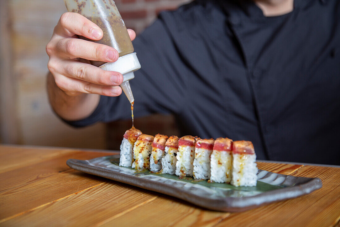 Koch beträufelt Sushi-Rollen mit Sauce