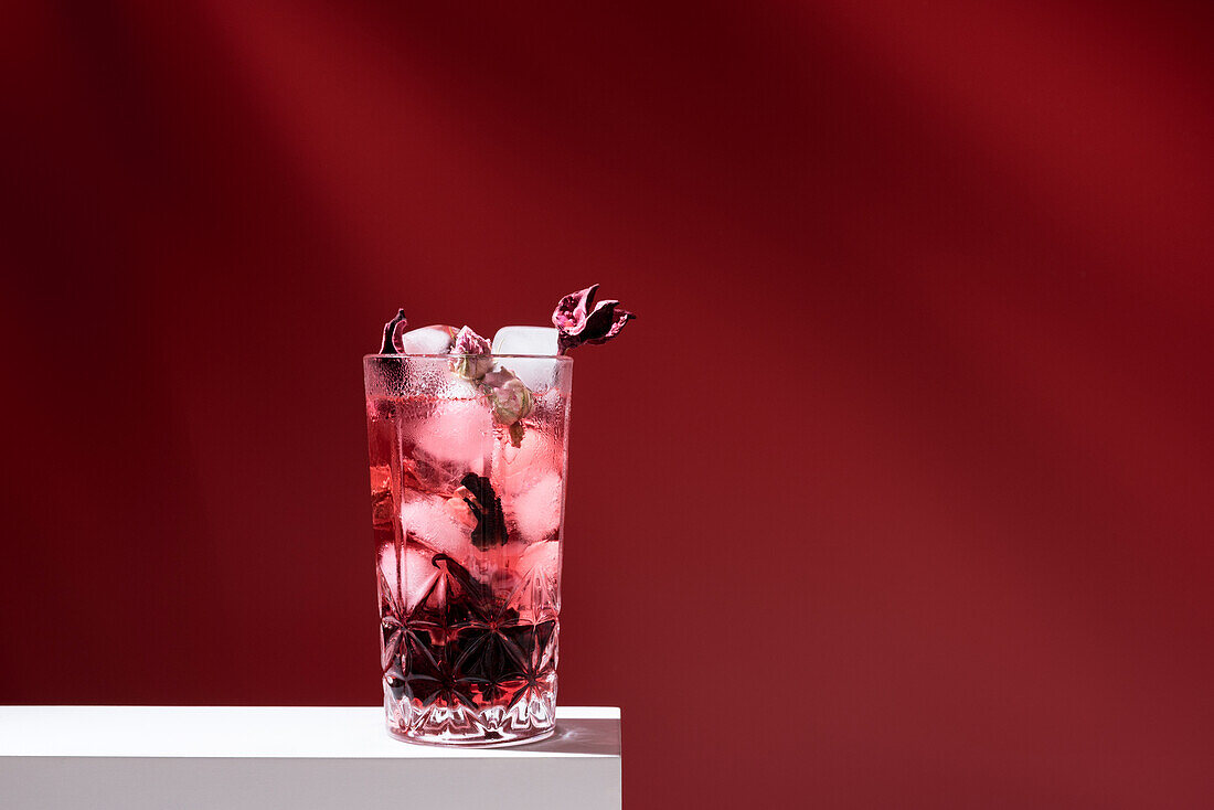 Glass filled with pink gin tonic and ice placed on white table against red background