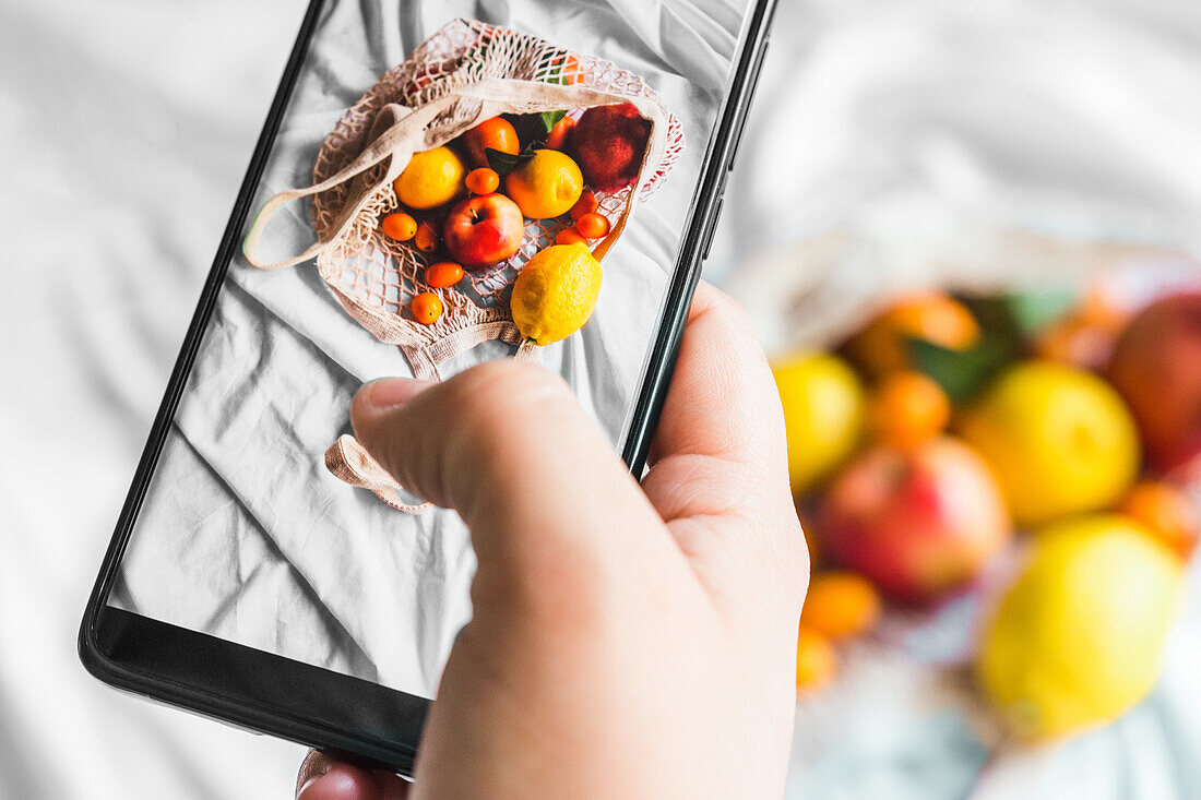 Frisches Obst in Einkaufsnetz mit Smartphone fotografieren