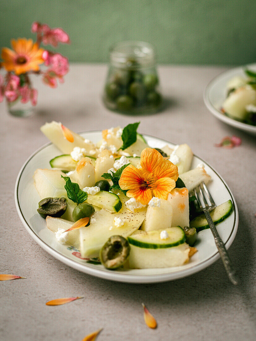 Melon salad with cucumbers and olives served on plate with herbs near salt shaker and napkin