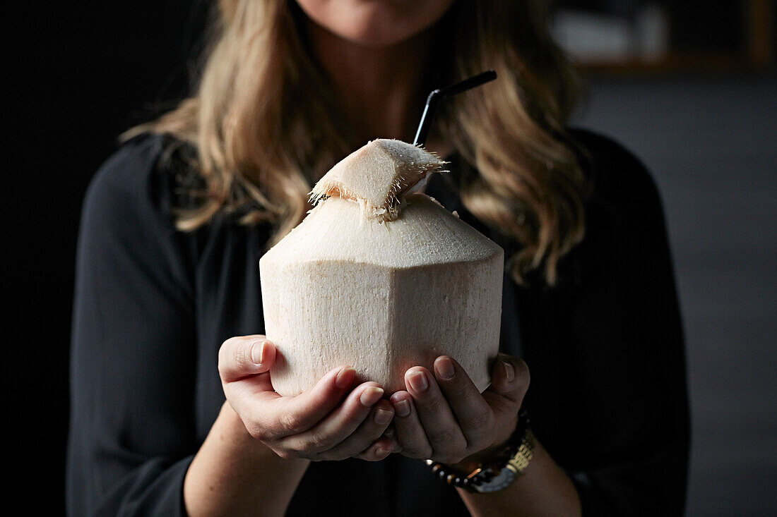 Frau hält trinkfertig geschnittene Kokosnuss in den Händen