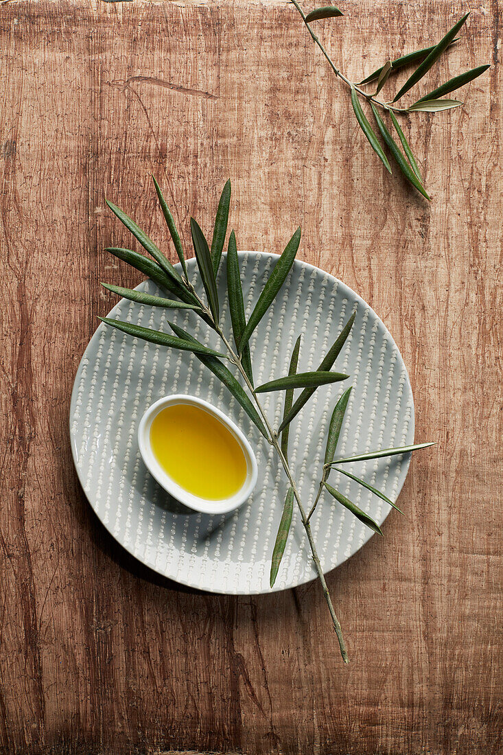 Olive oil in a small bowl with an olive sprig on a plate