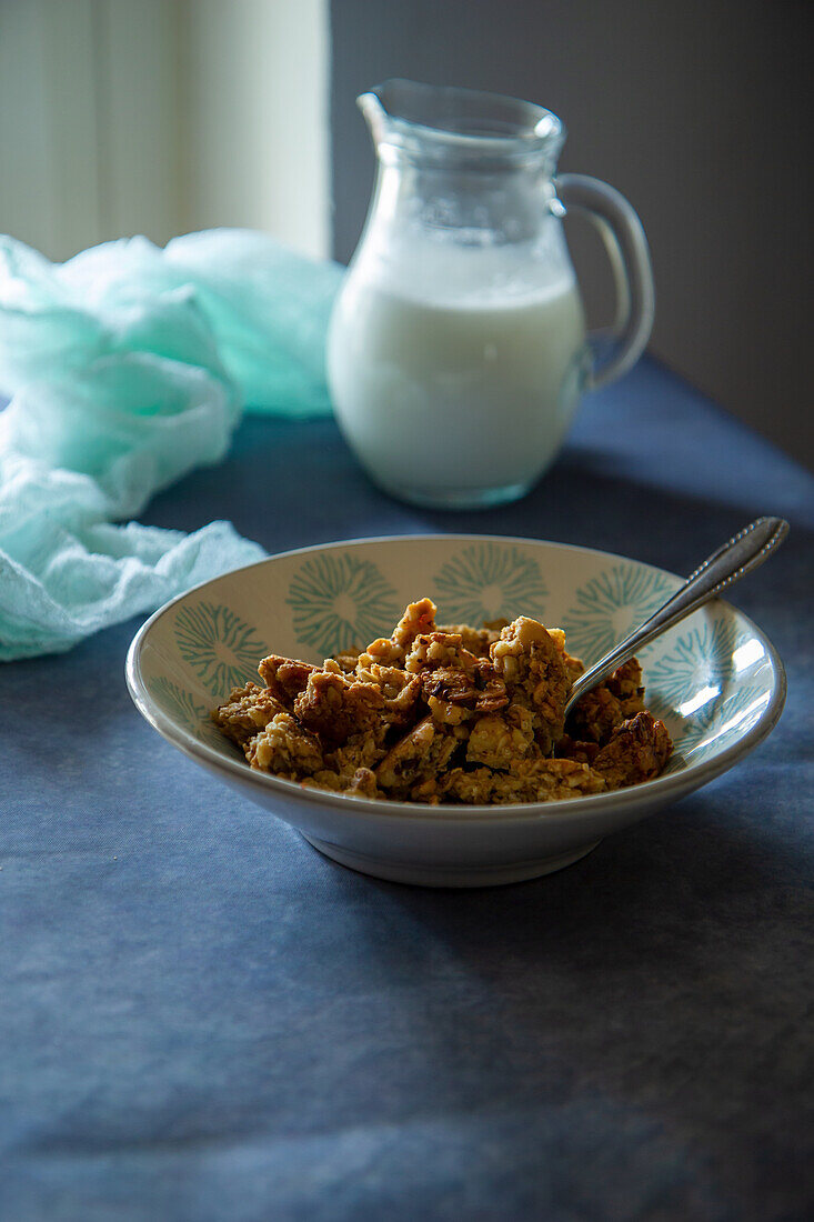 Granola in a bowl behind milk in a pitcher