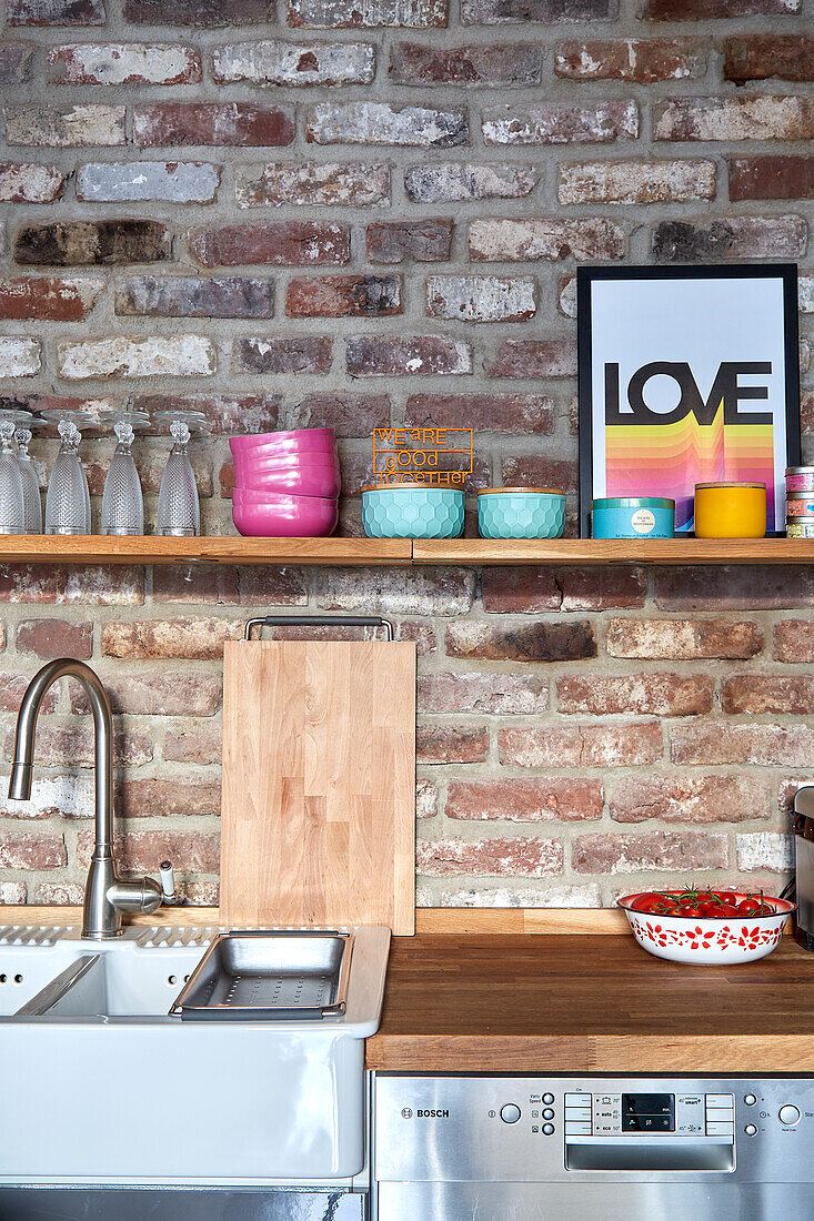 Kitchen corner with open shelving on brick wall and colourful decorative elements