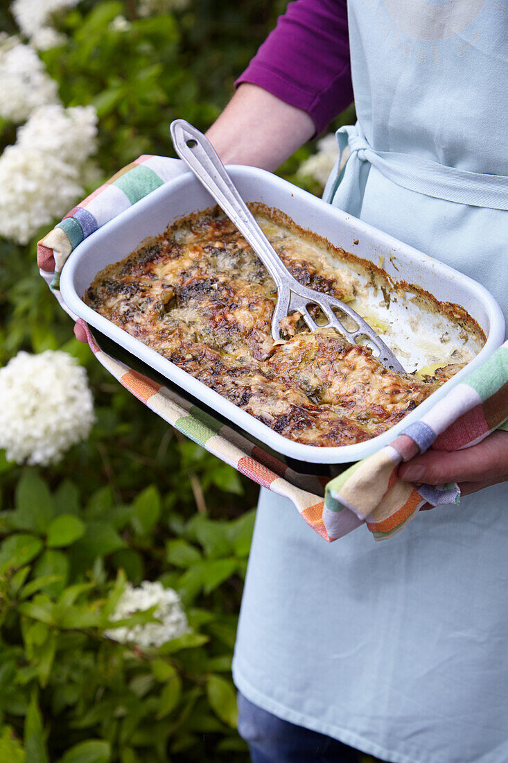 Woman holding oven dish with wild herb potato casserole in her hands