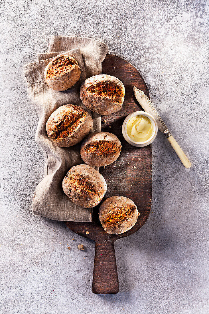 Wholemeal roll and a small bowl of butter on a wooden board