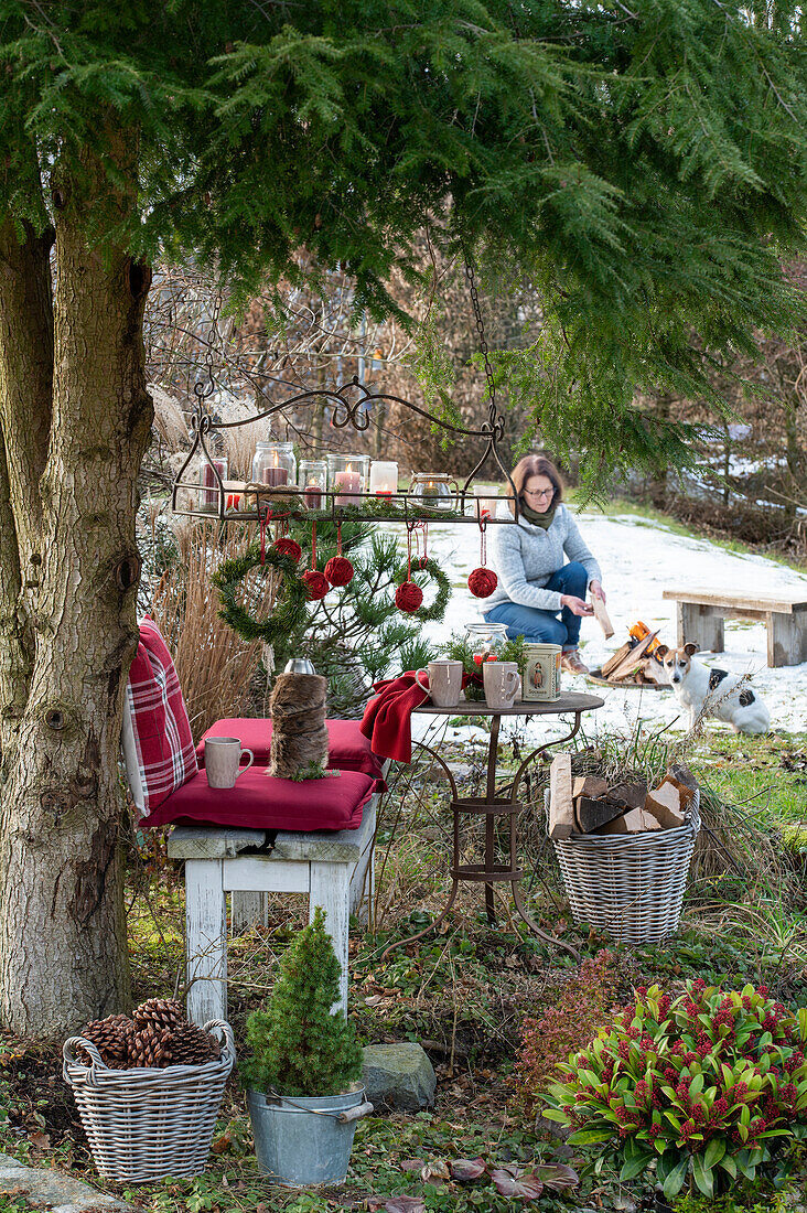 Christmas place in the garden - with cushion, hanging tray, lanterns and Christmas tree balls wrapped with jute string, woman in the background