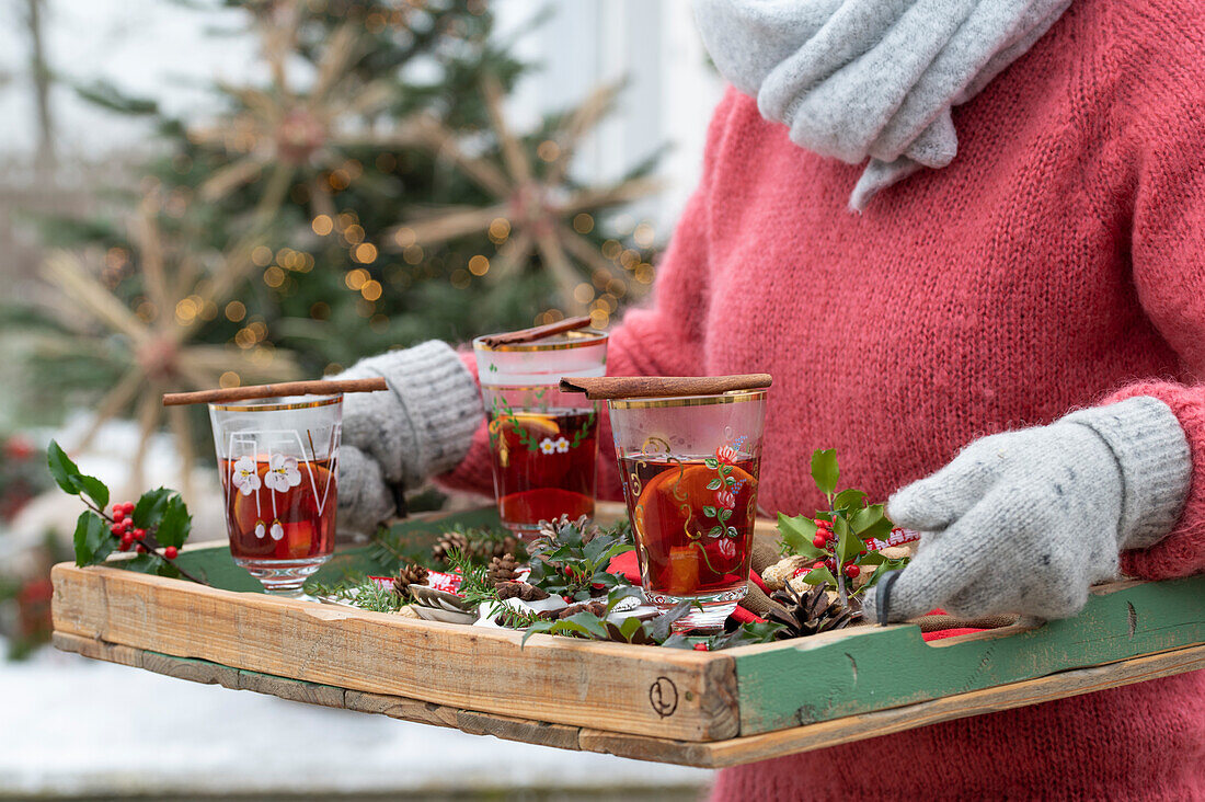 Hände mit Handschuhen halten Holztablett mit Punsch und Weihnachtsdekoration