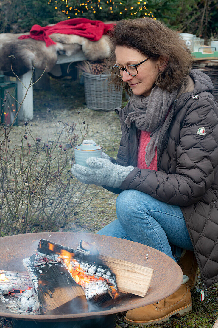 Woman with a cup of mulled wine squating around a fire pit