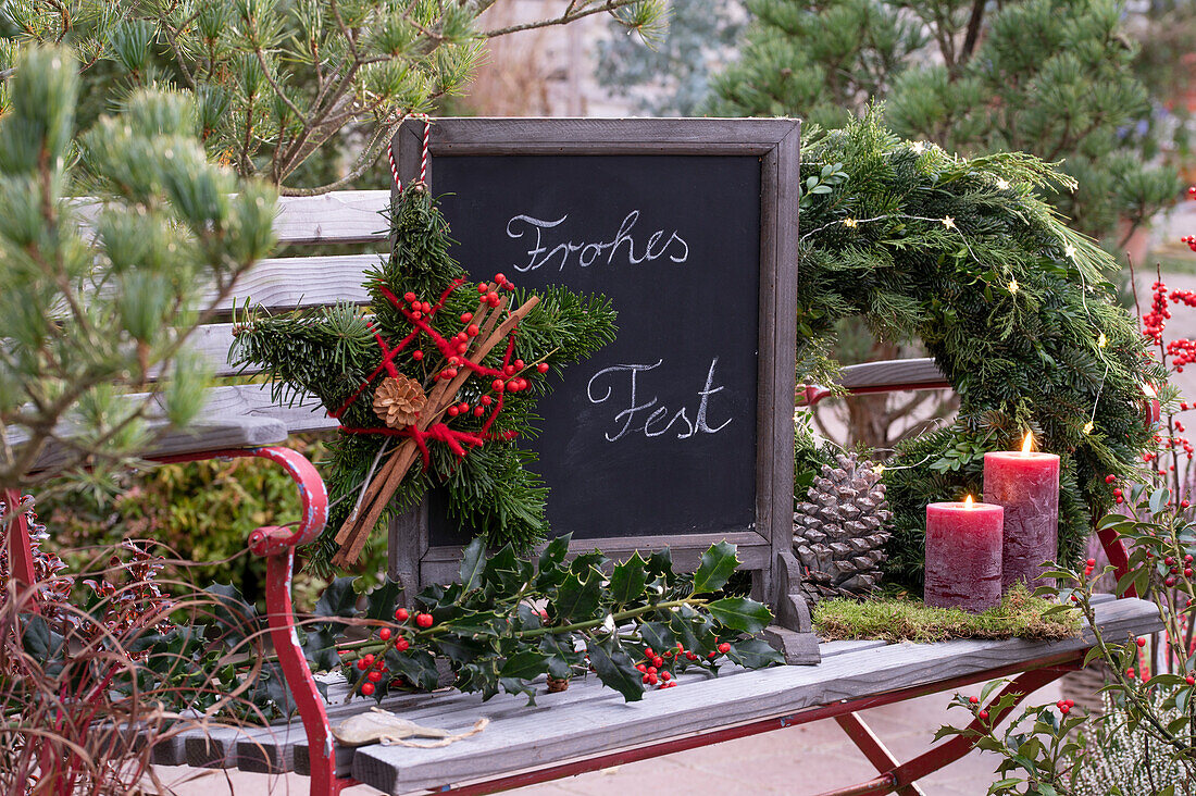 Star made of fir branches, holly branch and slate board with Christmas greeting on garden bench