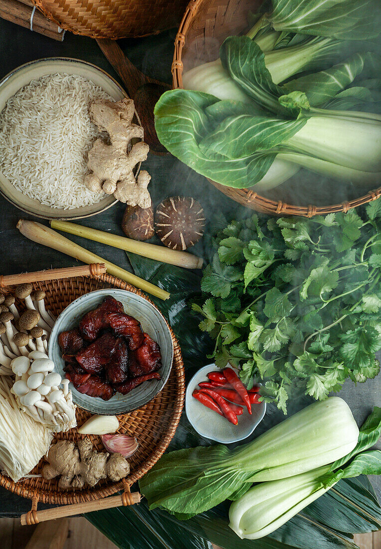 Ingredients for Asian cuisine in a bamboo steamer (rice, Asian mushrooms, shiitake, Shimeji, pak choi, bamboo leaves, ginger, chili)