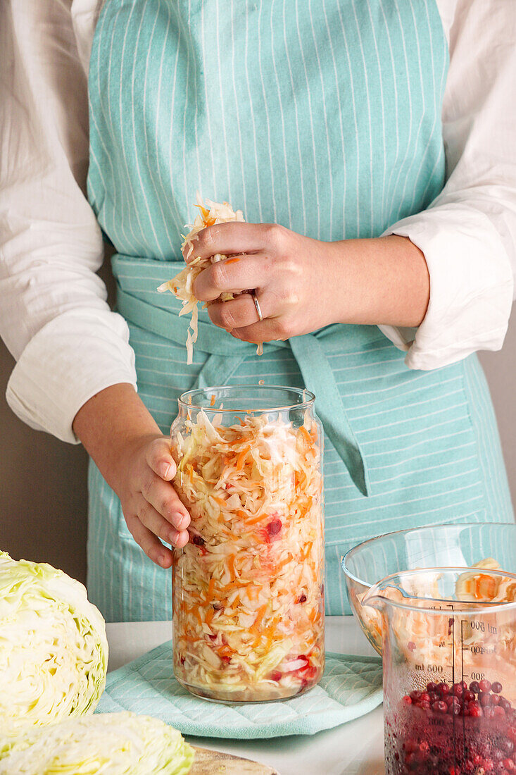 Cabbage fermented - woman packing into glass jar on table in kitchen
