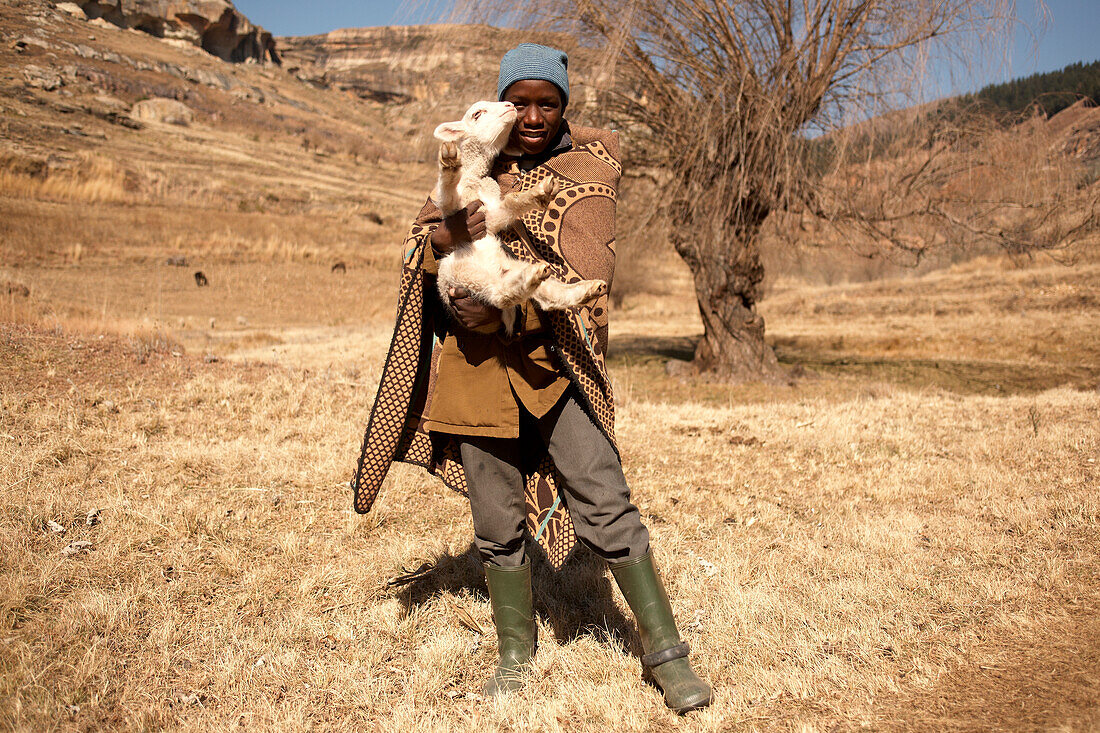 Einheimischer Hirte des Basotho-Volkes mit einem Lamm im Hochland, Königreich Lesotho, Südafrika