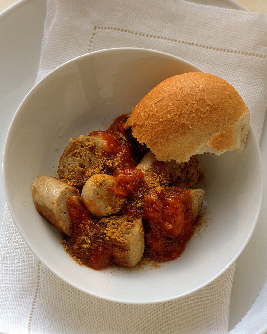 Chopped curry sausage and piece of roll in bowl