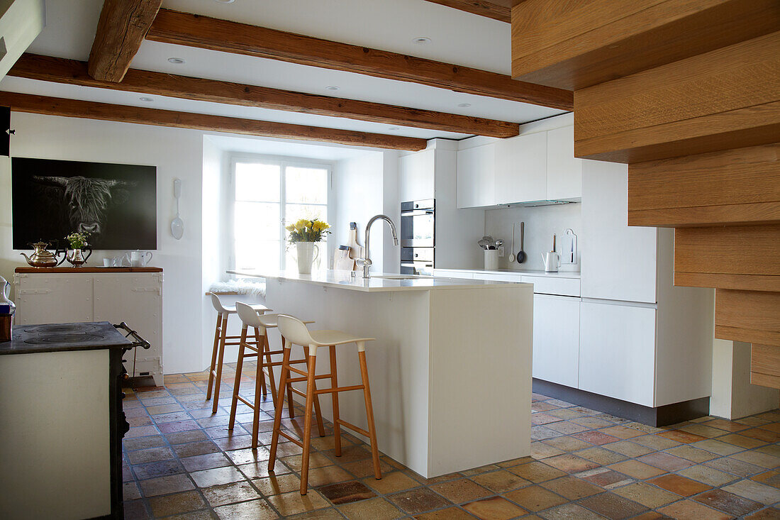 White kitchen counter with bar stools in light-colored kitchen