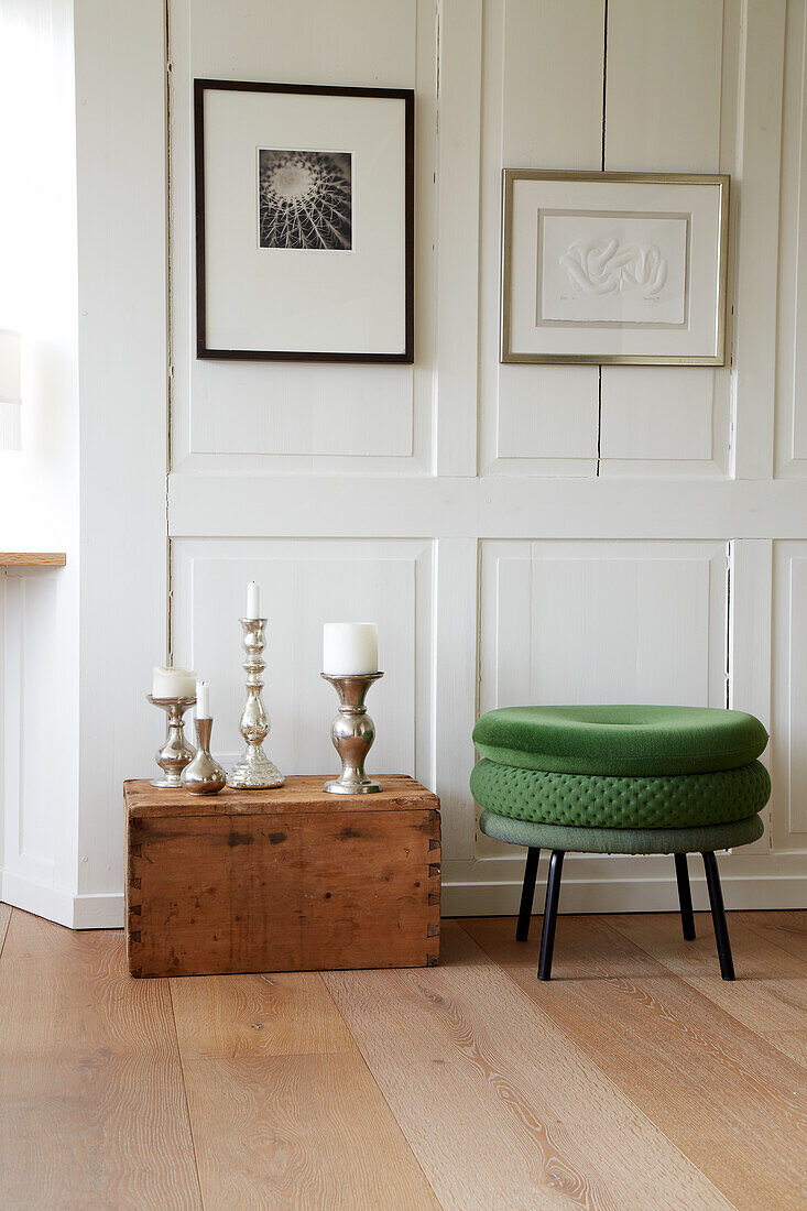 Green stool, wooden box and candlestick in front of white panelled wall