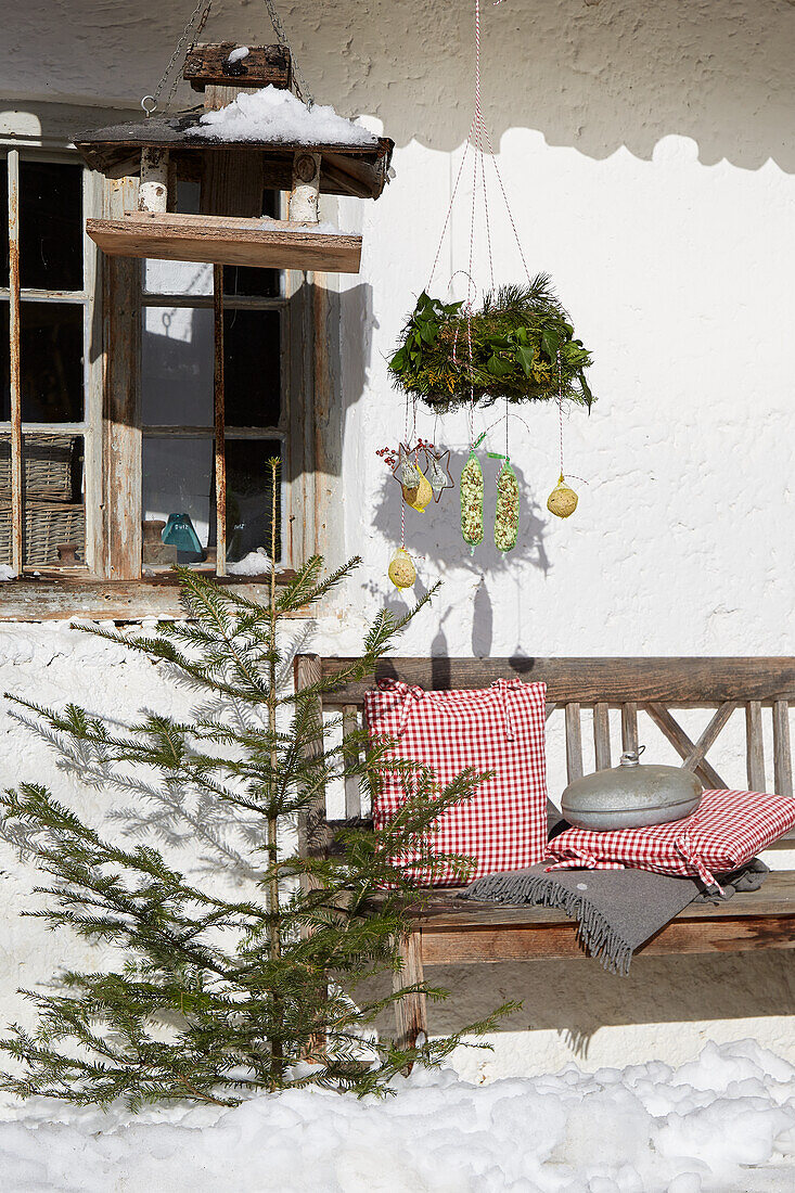 Rustic wooden bench with checkered cushions and winter decoration in the snow