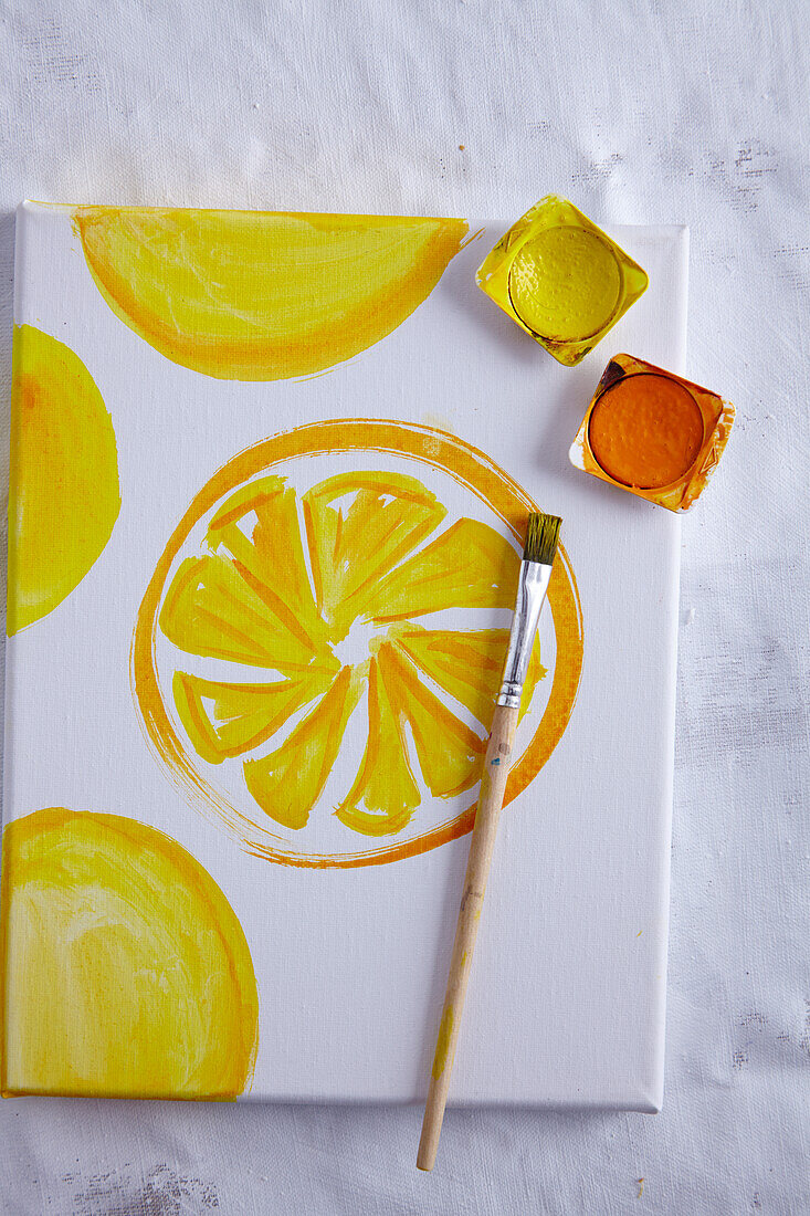 A small canvas with a lemon slice motif, watercolours and a brush (stimulating scents)