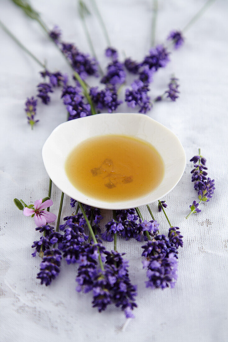 Schälchen mit Aromaöl, umgeben von Lavendelblüten (für Entspannungsbad)