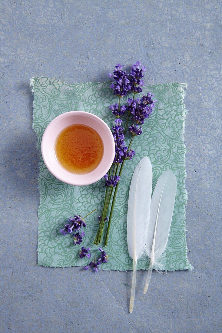 Honey in a small bowl, lavender and two white feathers (honey bath)