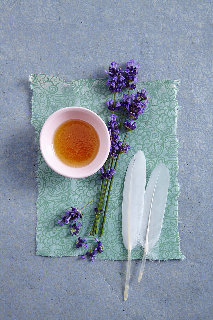 Honig in einem Schälchen, Lavendel und zwei weiße Federn (Honigbad)