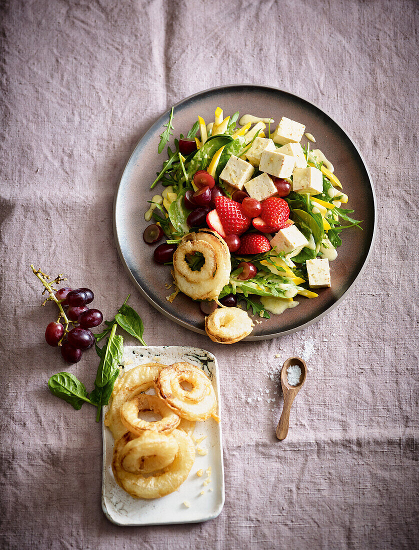 A salad with fried onion rings, feta, strawberries and grapes