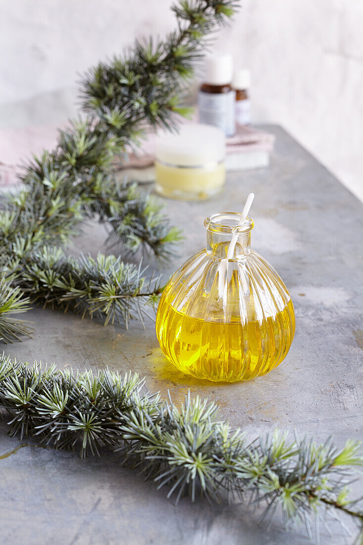 Glass jar with oil, a branch of Atlas cedar, in the background crucible and essential oil bottles