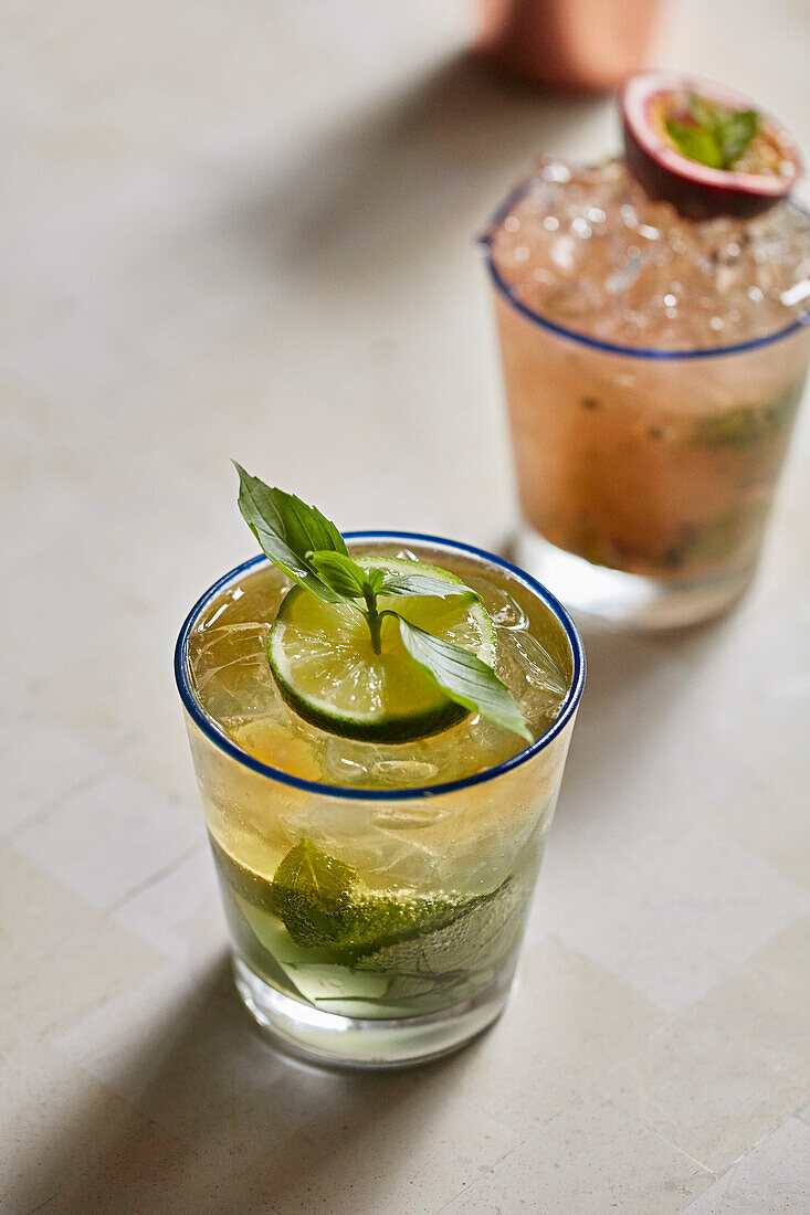 Two cocktails, one with a passionfruit and mint garnish and one with lime and mint