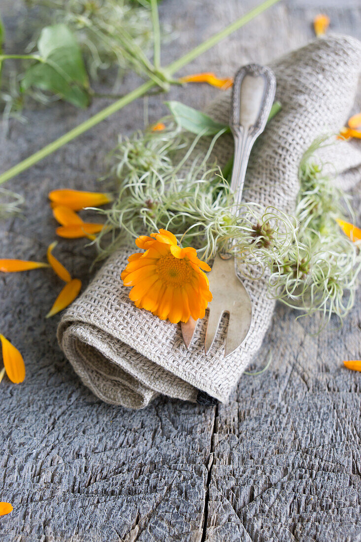 Leinenserviette mit Ringelblumen (Calendula officinalis), und Serviettenring aus Clematis-Fruchtständen