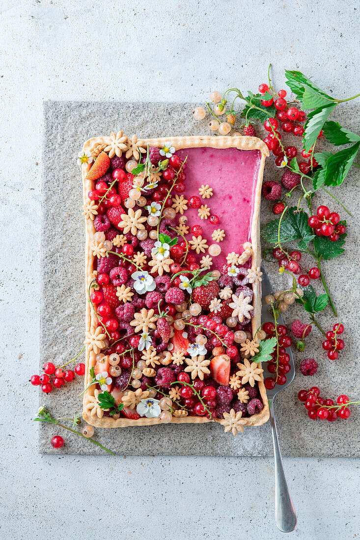 Himbeerkuchen dekoriert mit Beeren und blütenförmigen Plätzchen