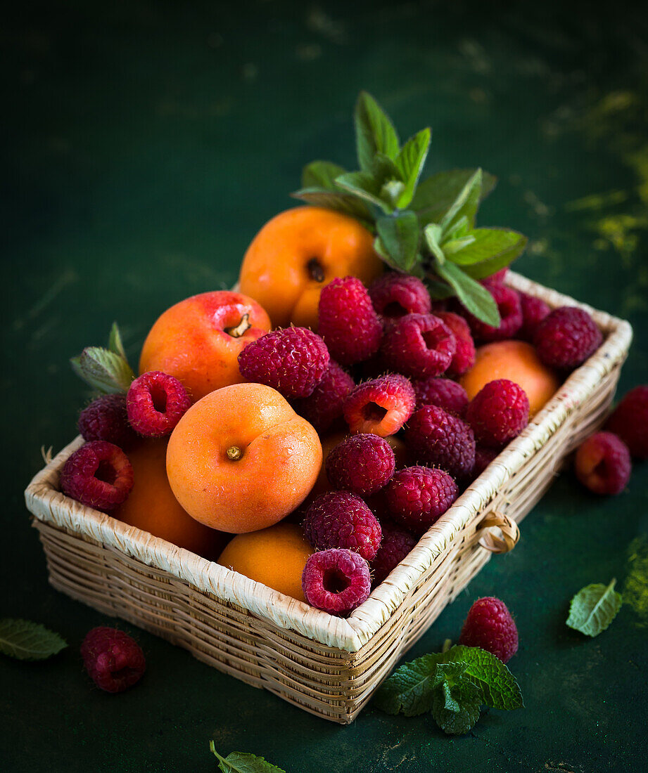 Kiste mit frischen Himbeeren, Aprikosen und Minze