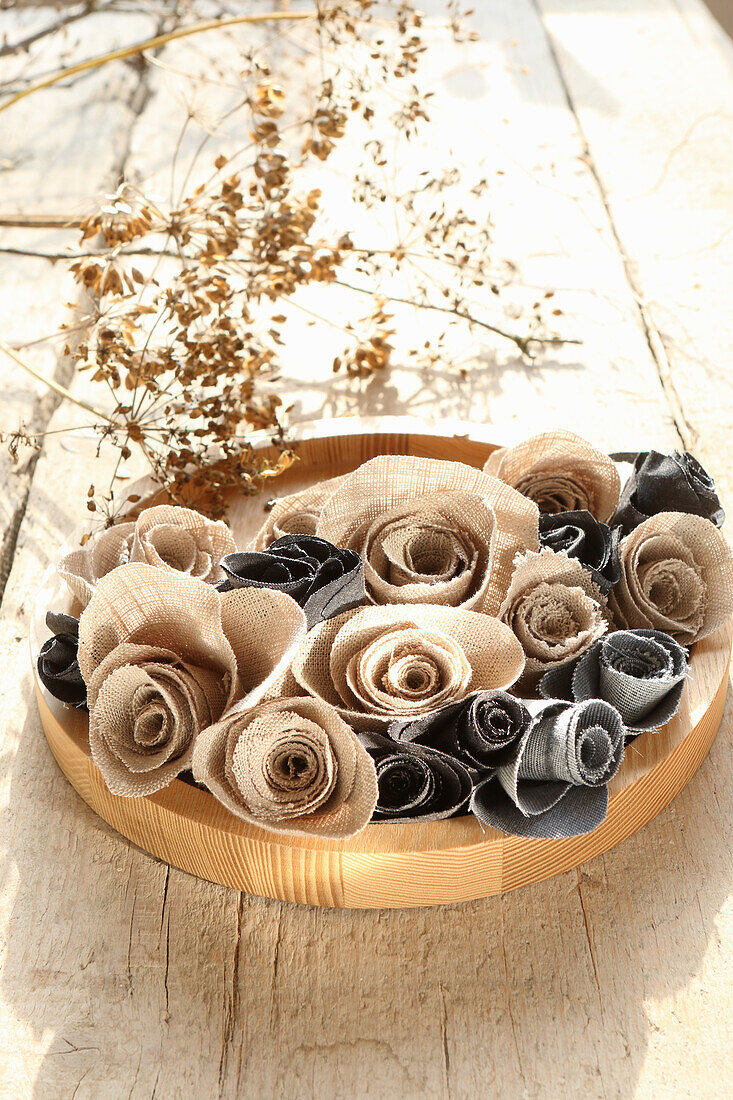 Beige and grey fabric roses on round wooden plate, dried grass in the background
