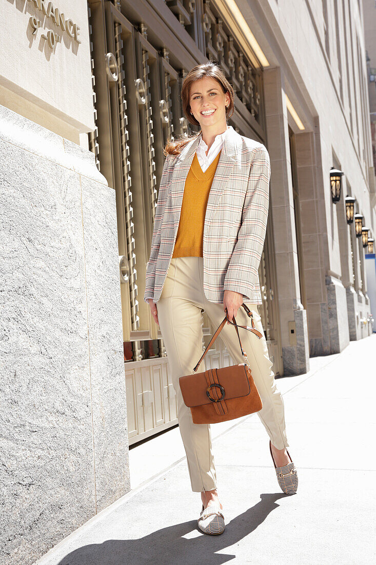 A brunette woman wearing a mustard yellow jumper, a light blazer and trousers