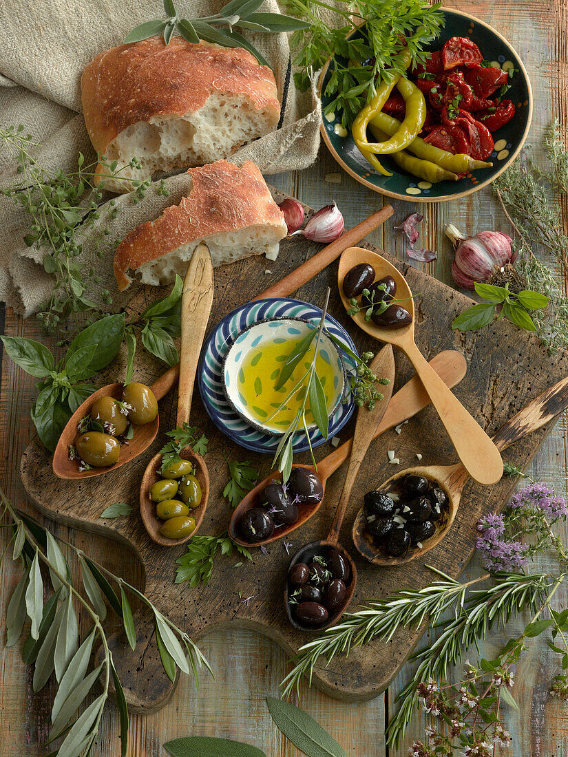 Stillleben mit eingelegten grünen und schwarzen Oliven auf Holzlöffeln, getrockneten Tomaten und Chili