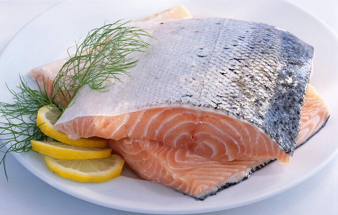 Two pieces of salmon with skin, lemon, and dill on a white plate