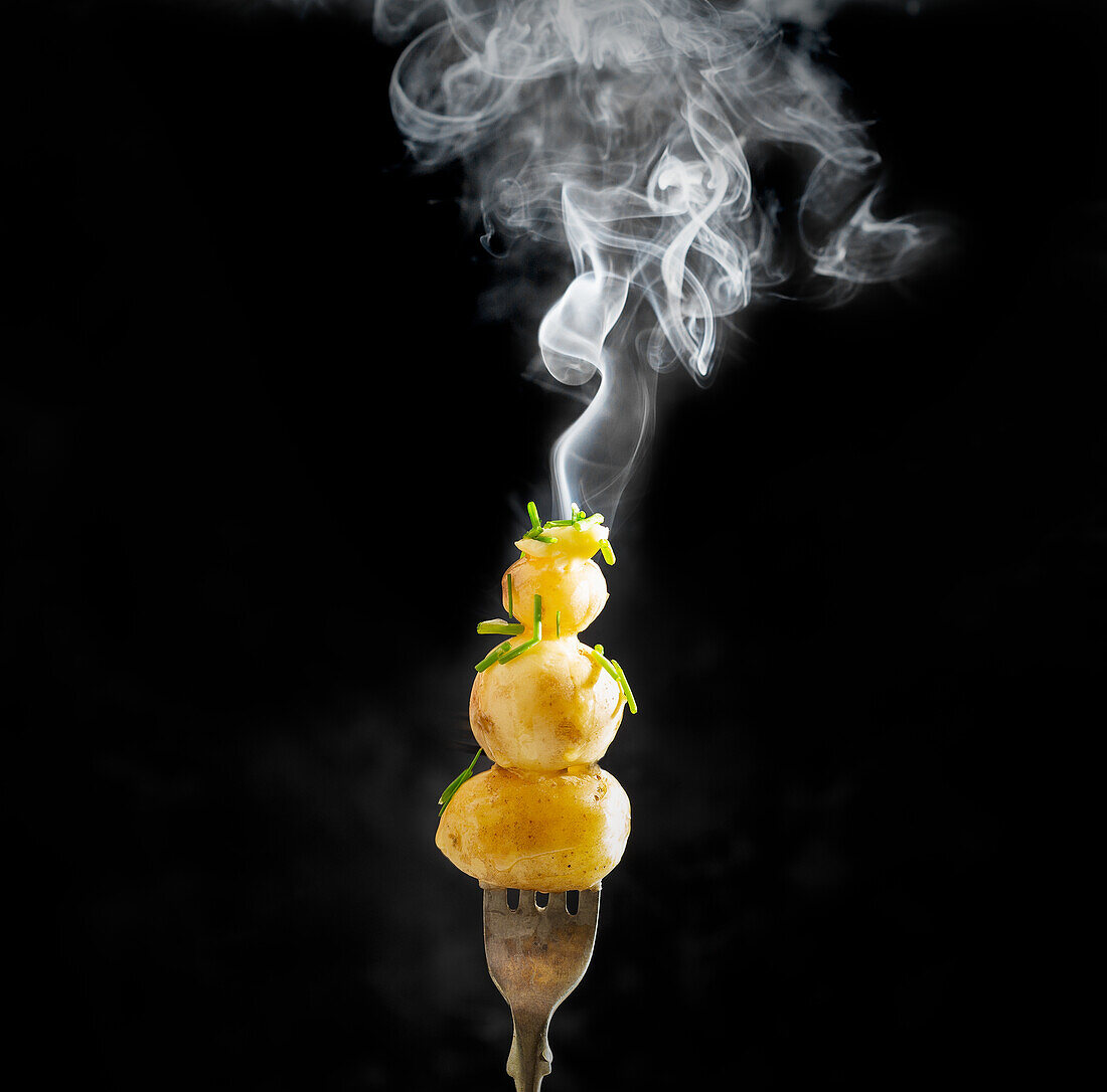 Steaming baby potatoes with buttered chives skewered on a fork