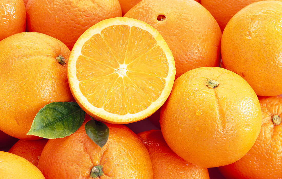 Mehrere Apfelsinen und eine Apfelsinenhälfte (Bildfüllend)