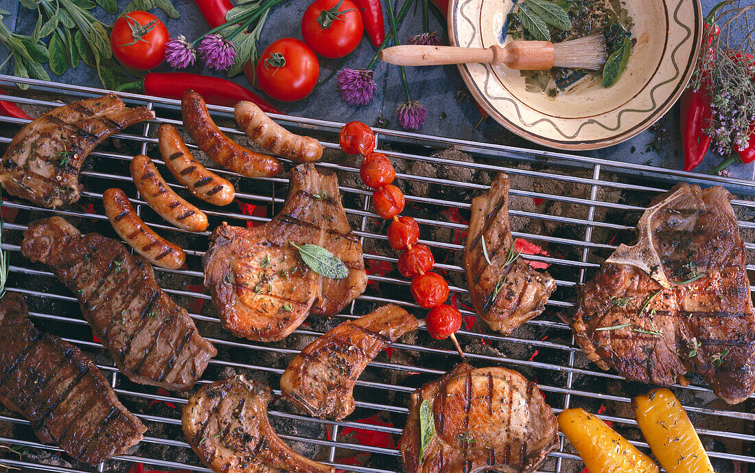 Grilled sausages, lamb chops, pork chops, steaks and tomatoes on a grill rack