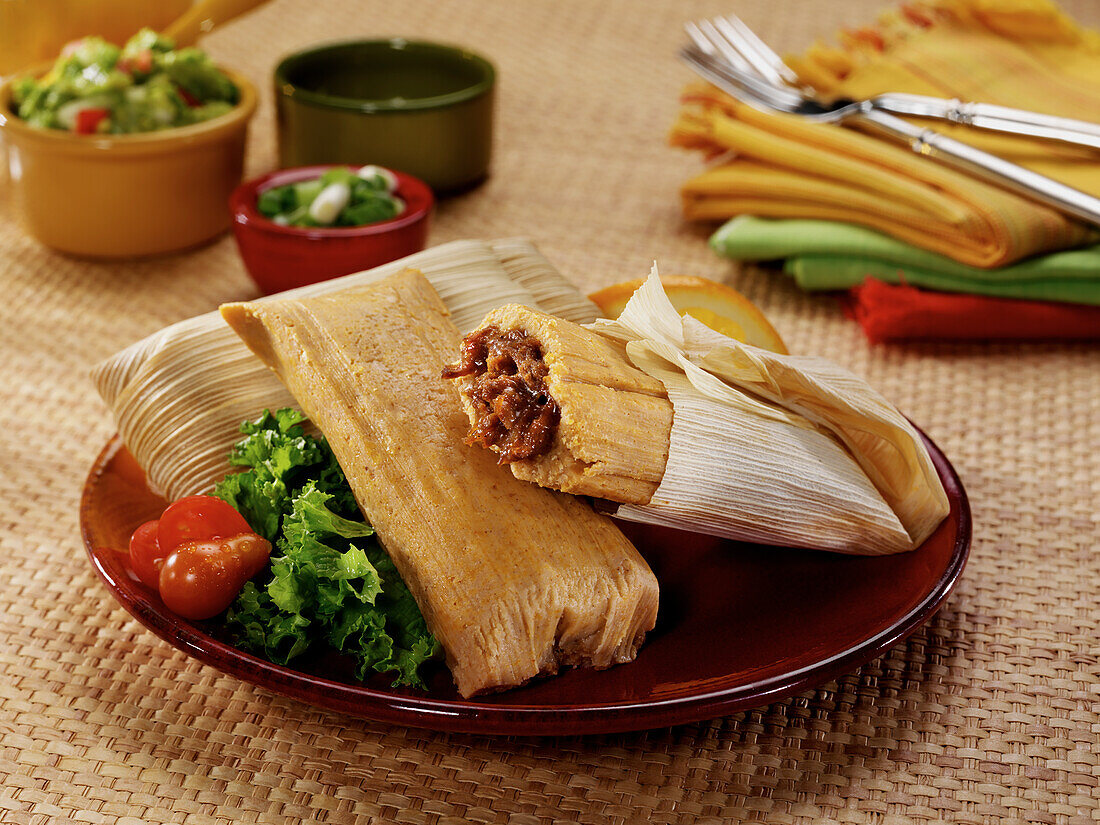 Mexican pork tamales steamed in corn husks with lettuce and tomato in a casual setting