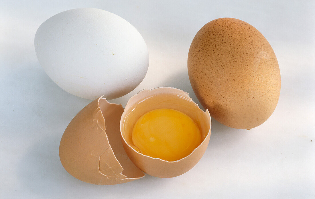 One white egg, one whole brown egg and one cracked brown egg on a light background