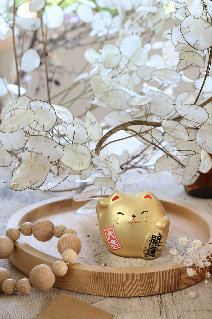 Golden lucky cat on a wooden plate with dried flower Lunaria in the background