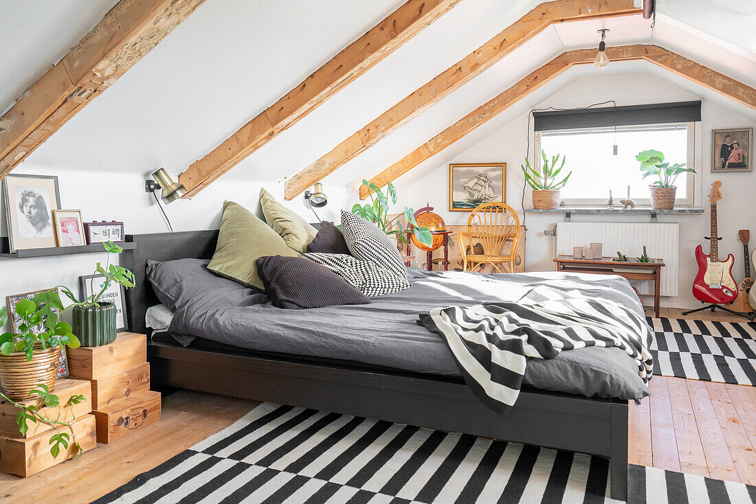 Holzkisten mit Zimmerpflanzen neben grauem Doppelbett in weißem Dachgeschoss-Gästezimmer