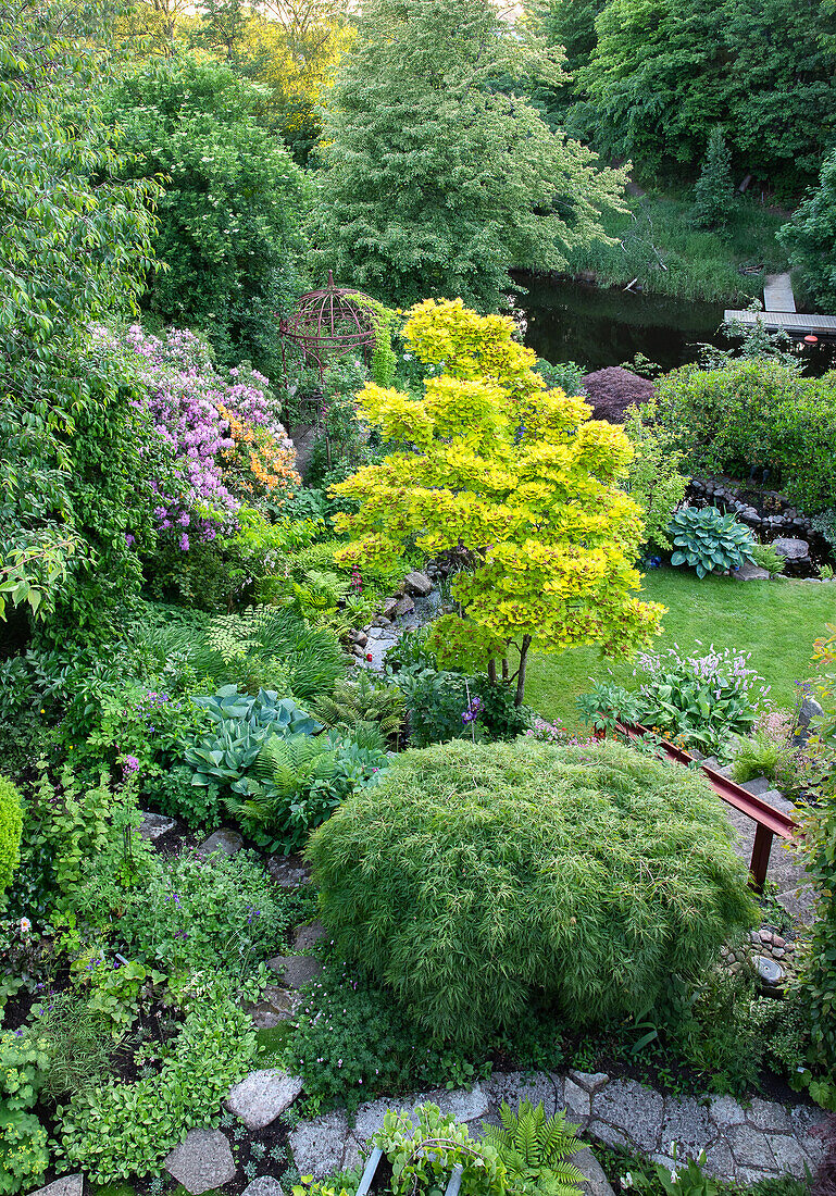 Blick auf vielfältig bepflanzten Garten mit Teich im Frühling