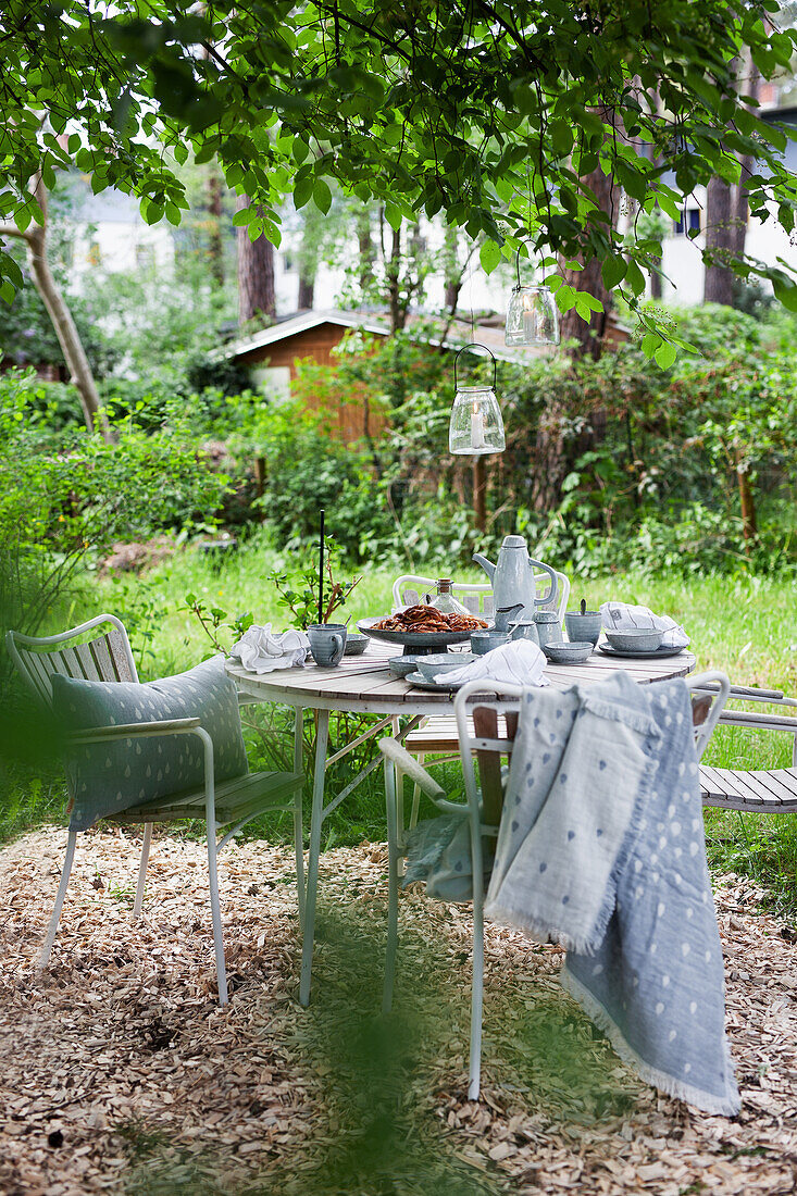 Runder Kaffeetisch mit zwei Stühlen unterm Baum im Garten