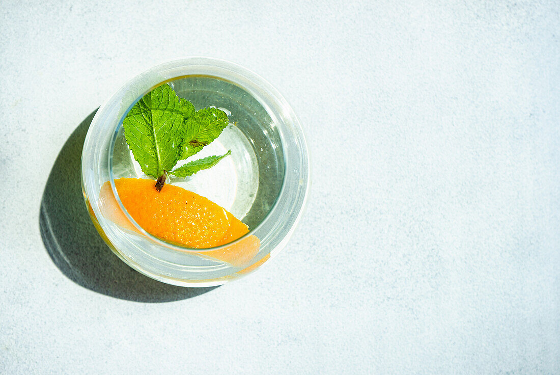 Glass of refreshing water with orange and mint in sunny day